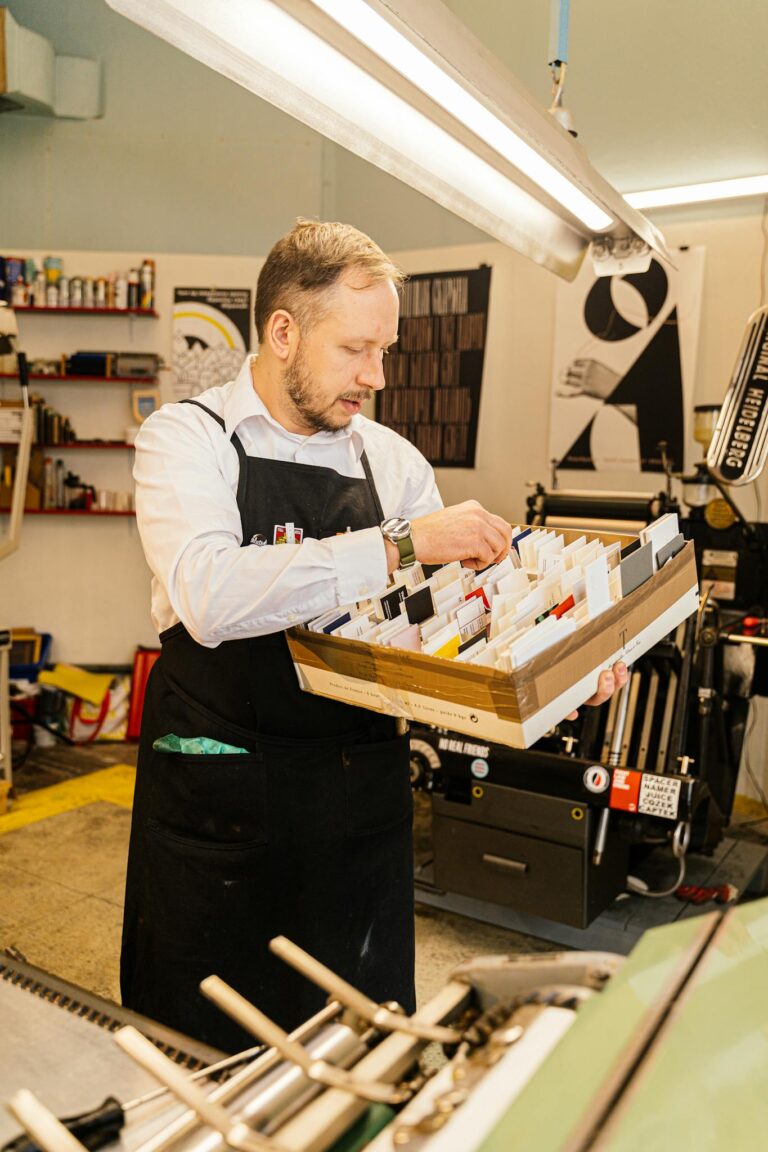 A Man in White Long Sleeves Wearing Black Apron Looking at the Cards on the Box